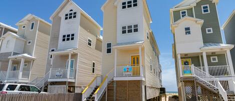 A row of beach houses with balconies, wooden decks, and a sandy beach in the background.