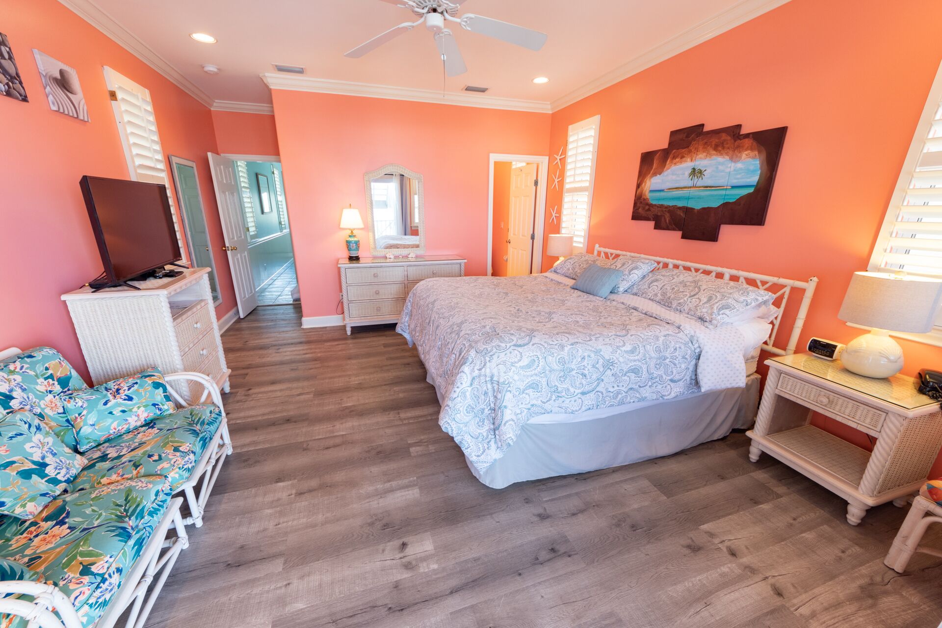 A bedroom with a large bed, a television, a desk, a chair, and a window with shutters.