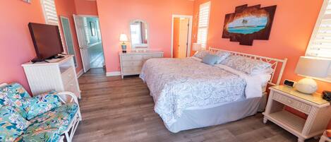 A bedroom with a large bed, a television, a desk, a chair, and a window with shutters.