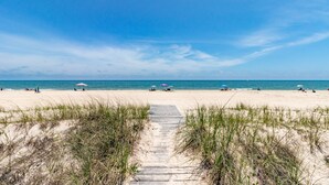 Une plage avec une promenade en bois menant à la mer, entourée de sable et d’une végétation clairsemée.