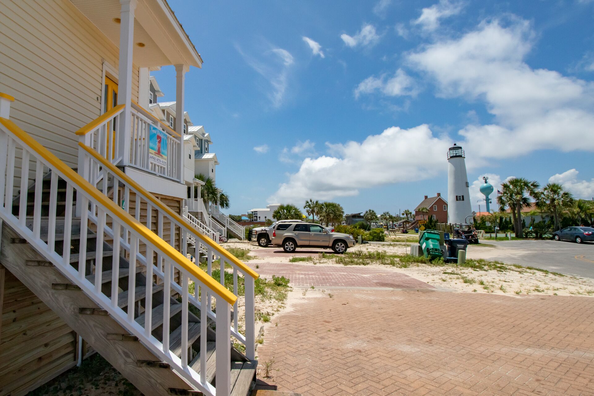 A coastal building with a staircase, a parked SUV, and a lighthouse in the background.