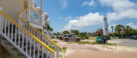 A coastal building with a staircase, a parked SUV, and a lighthouse in the background.