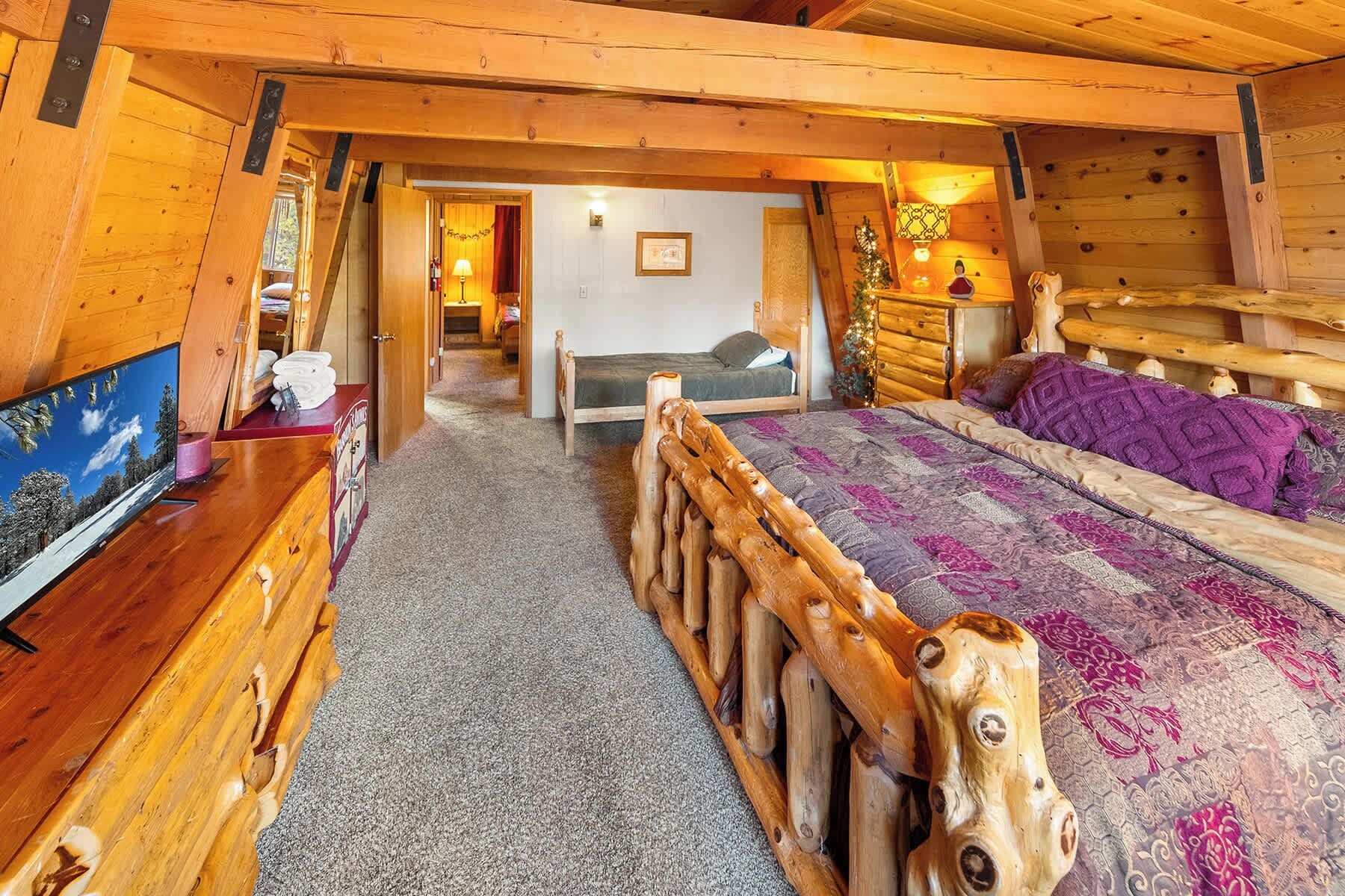 Un dormitorio rústico de cabaña con estructura de cama de madera, televisor y un escritorio pequeño.