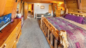 Un dormitorio rústico de cabaña con estructura de cama de madera, televisor y un escritorio pequeño.