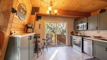 A kitchen with wooden walls, a chandelier, a coffee maker, and a view of the outdoors.