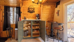 Interior acogedor de una cabaña con techo de madera, un candelabro, una estación de café y un comedor con mesa y sillas.