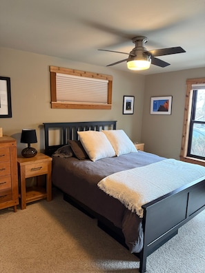A bedroom with a bed, a nightstand, a lamp, a ceiling fan, and a window.