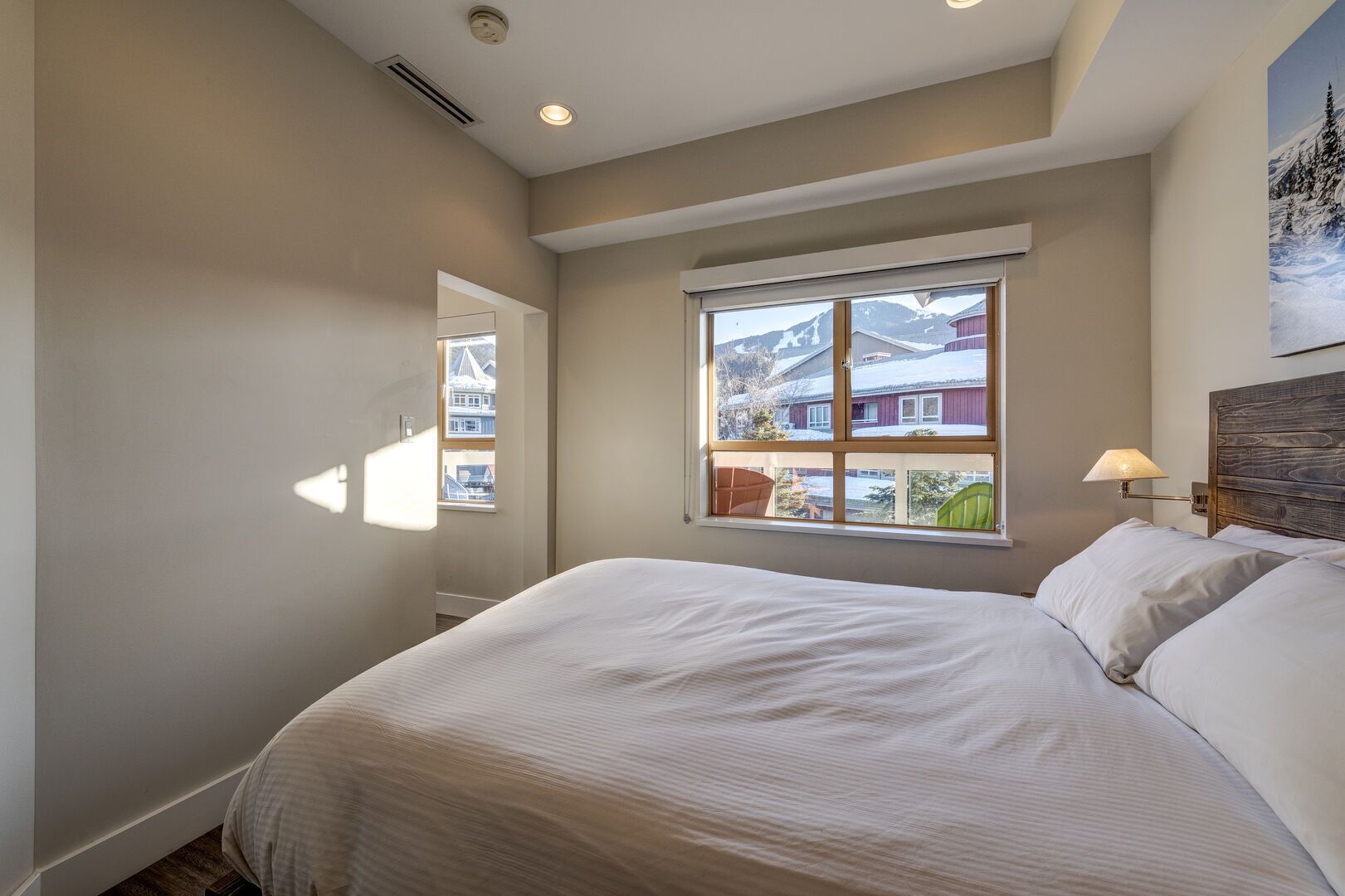 Een slaapkamer met een groot bed, een raam met uitzicht op gebouwen en bergen, en een wandlamp.