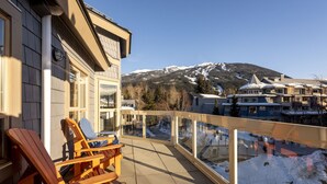 Ein Balkon mit Holzkubeln, einer Glasufernung und Blick auf verschneite Berge und Gebäude.