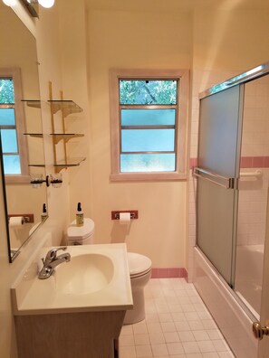 Bathroom features a sink, mirror, toilet, and shower area with a glass door.