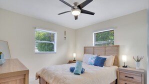 Ein Schlafzimmer mit Bett, Nachttischen, Deckenventilator und Fenstern mit Jalousien.