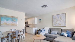A modern living room with a dining area, a grey sofa, and a kitchen in the background. - Crystal Sands Beach House in IRB! Great location 2/1 (Indian Rocks Beach)