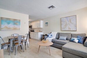 Een moderne woonkamer met een eethoek, een grijze bank en een keuken op de achtergrond.
