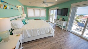 A bedroom with a bed, a desk, a TV, and a view of the outside.