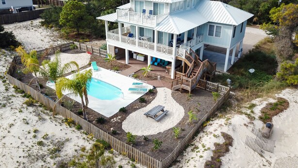 A two-story house with a large deck, a swimming pool, and a sandy beach area.