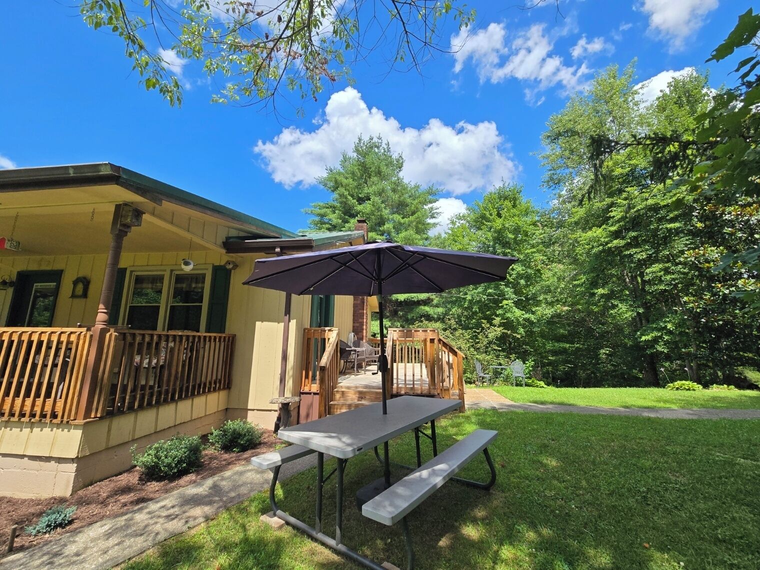 A covered patio with a table and bench, a wooden deck, and a house with a porch.