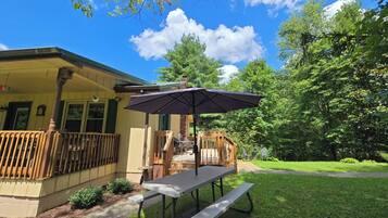 A covered patio with a table and bench, a wooden deck, and a house with a porch.