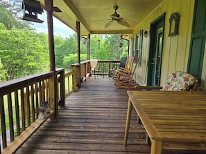 Une terrasse en bois avec une table et des chaises, un fauteuil à bascule et un ventilateur de plafond.