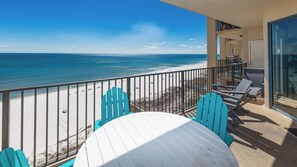 Varanda com vista para a praia e oceano, com mesa e cadeiras.