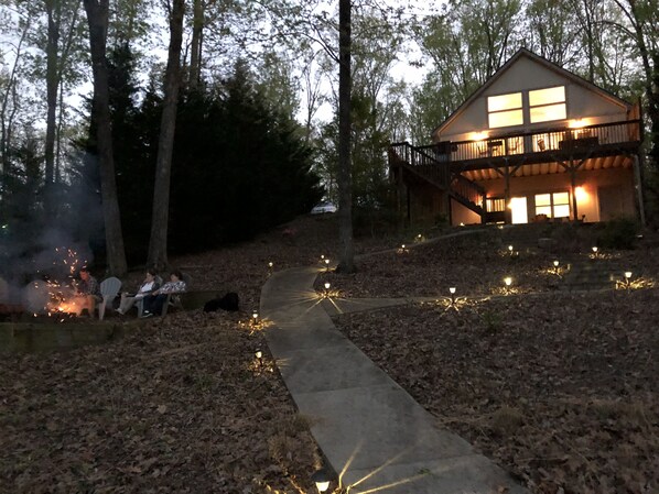 A cabin with a balcony, surrounded by trees and a fire pit area.