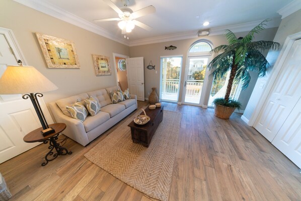 A spacious living room with a beige sofa, a coffee table, and a large potted plant. - BEACHFRONT in Casa Del Mar, 5BR/4.5BA, Sleeps 20, Elevator (St. George Island)