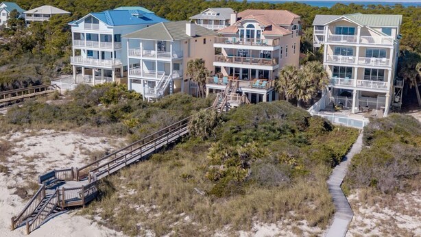 Une propriété située en bord de mer, avec des bâtiments à plusieurs étages, un escalier en bois menant à la plage et une vue dégagée sur l’océan.