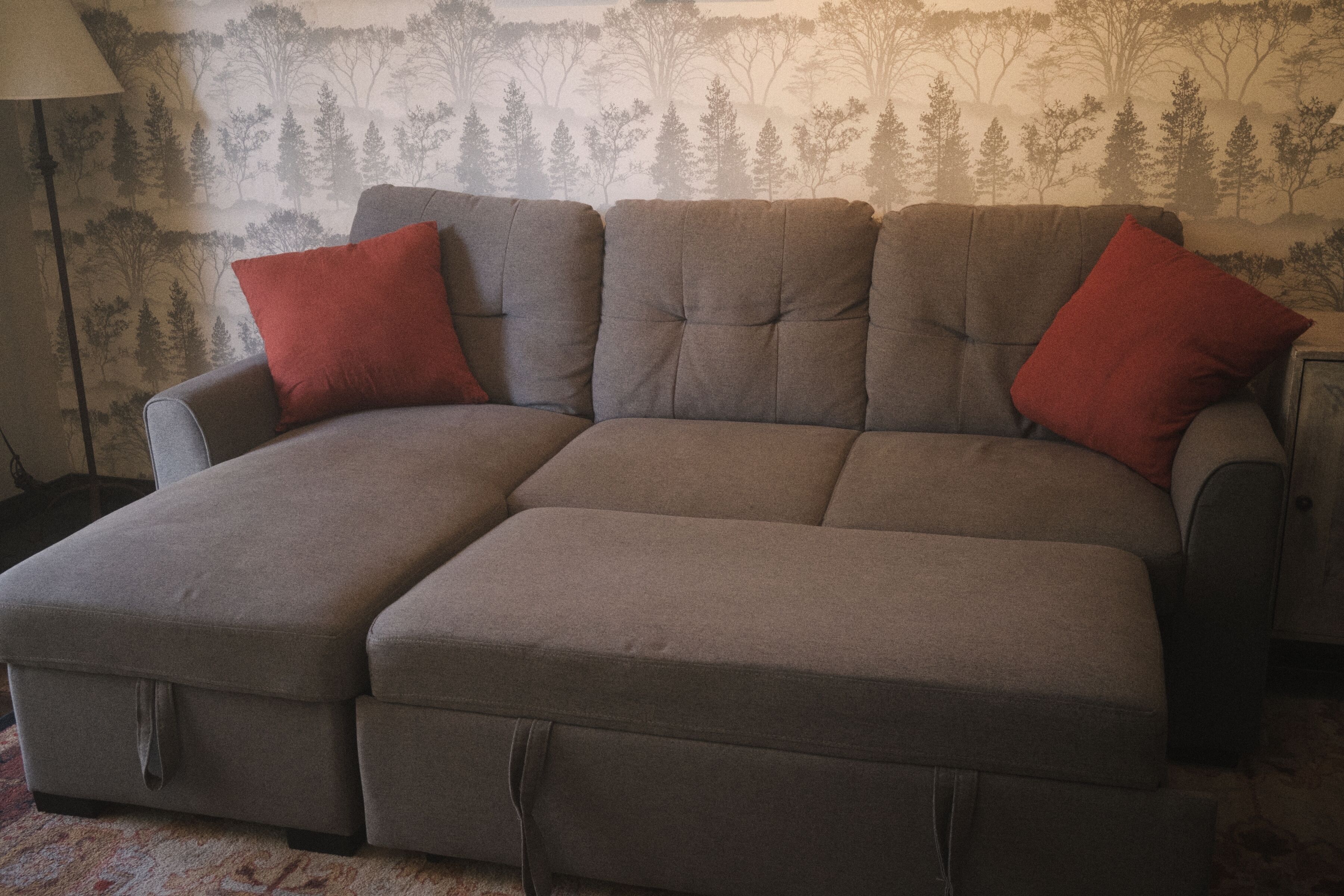 A sectional sofa with two red cushions, a lamp, and a patterned wallpaper background.