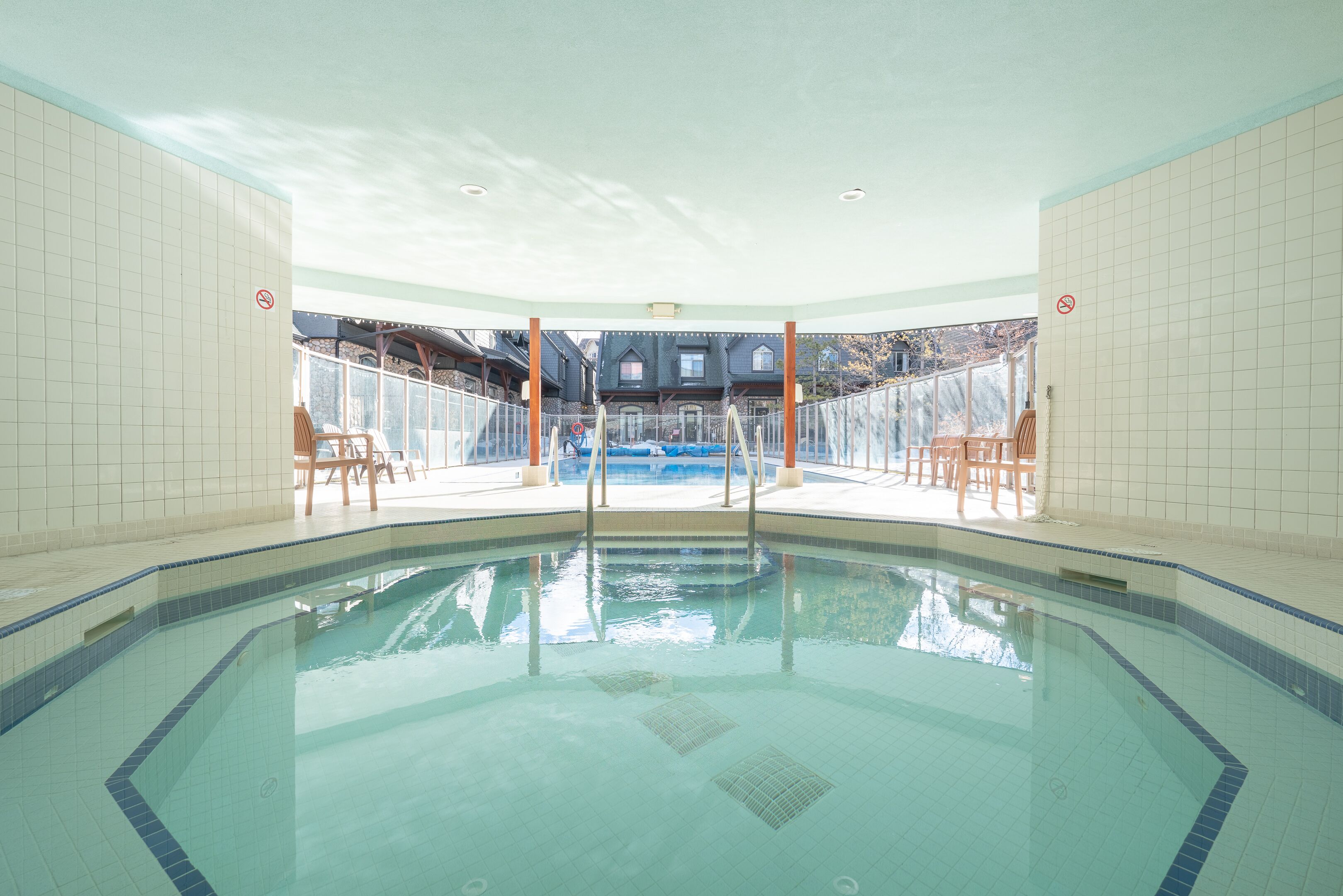 Una piscina interior con agua azul cristalina, rodeada de paredes de azulejos y sillas de madera.