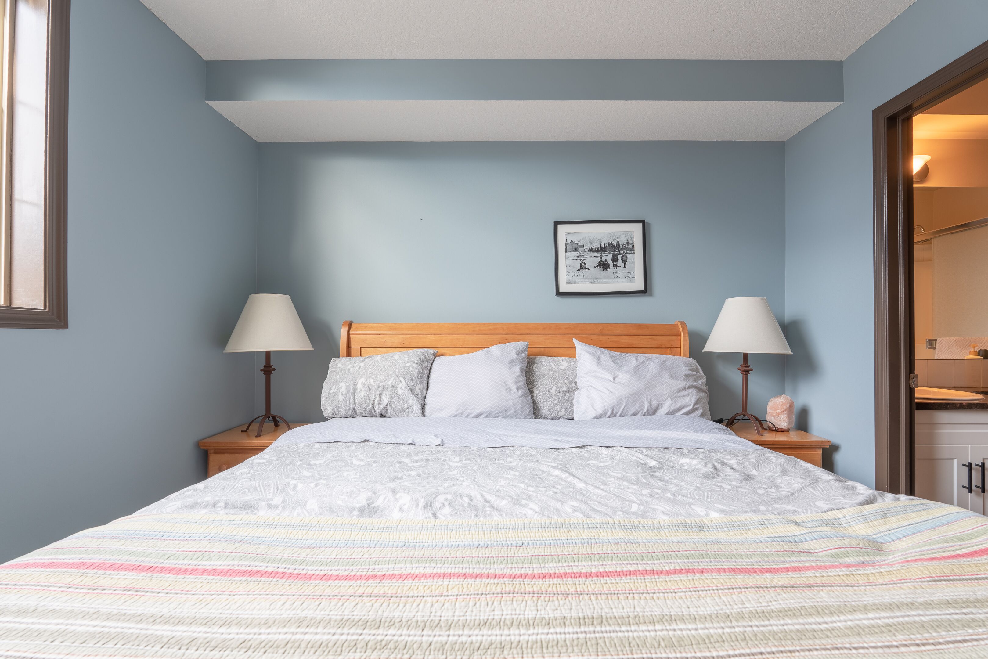A neatly made bed with a striped blanket, two bedside lamps, and a framed picture on the wall.
