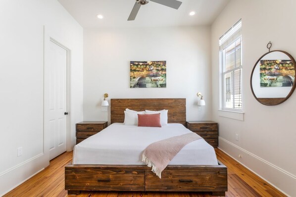 A bedroom with a wooden bed frame, white bedding, a ceiling fan, and two wall-mounted lamps. - 20% OFF Monthly | 10% OFF Weekly-Stylish 3BR on Carondelet by Hosteeva (New Orleans)