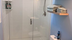 Et badeværelse med bruseniche i glas, toilet og håndvask.