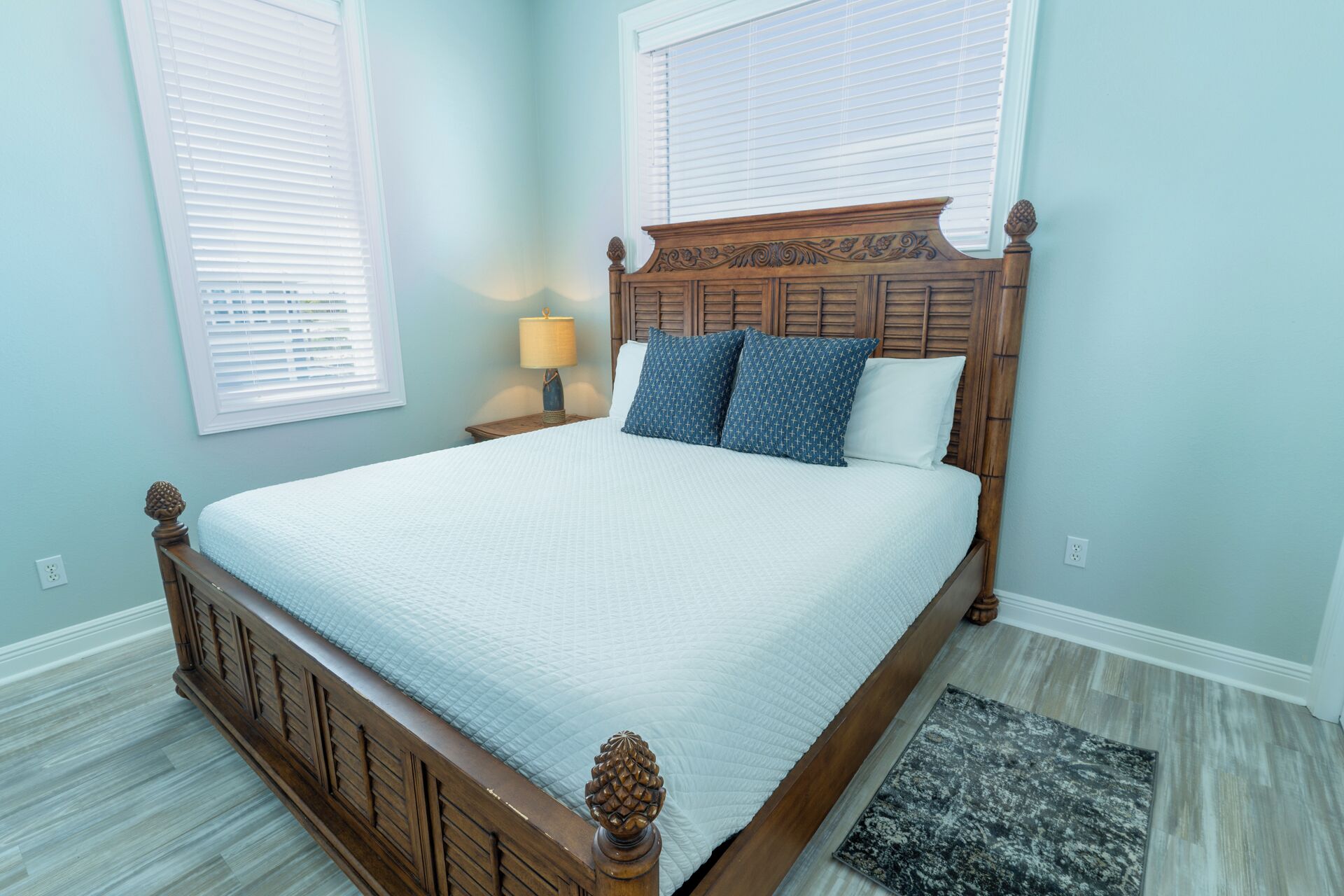 A bedroom with a wooden bed frame, two pillows, a bedside lamp, and a rug.
