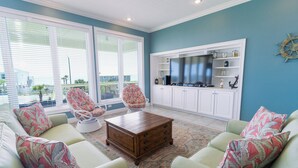 Un salón con televisor grande, armarios blancos y vistas al exterior a través de las ventanas.