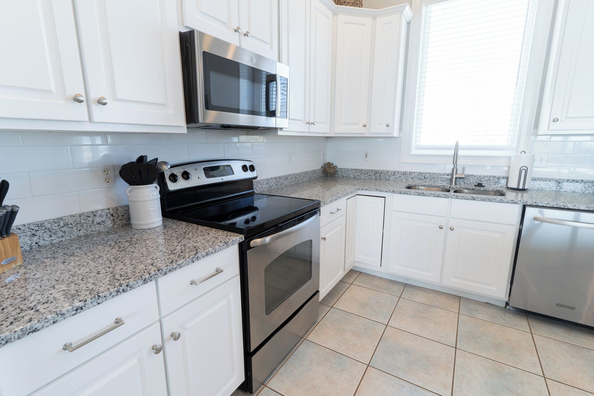 A kitchen with white cabinets, a stainless steel microwave, a black stove, a granite countertop, and a stainless steel sink.