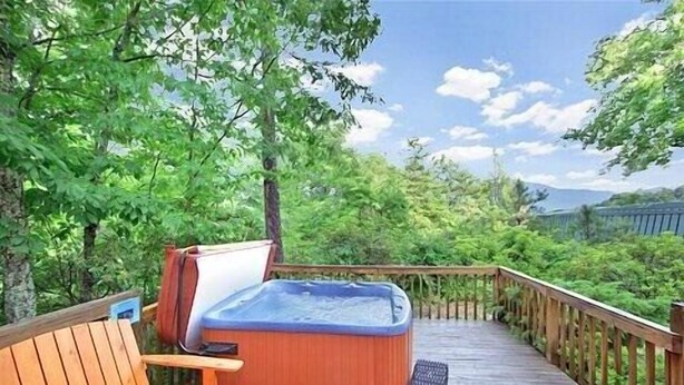 Una terraza de madera con jacuzzi, banco y vista a un área boscosa.