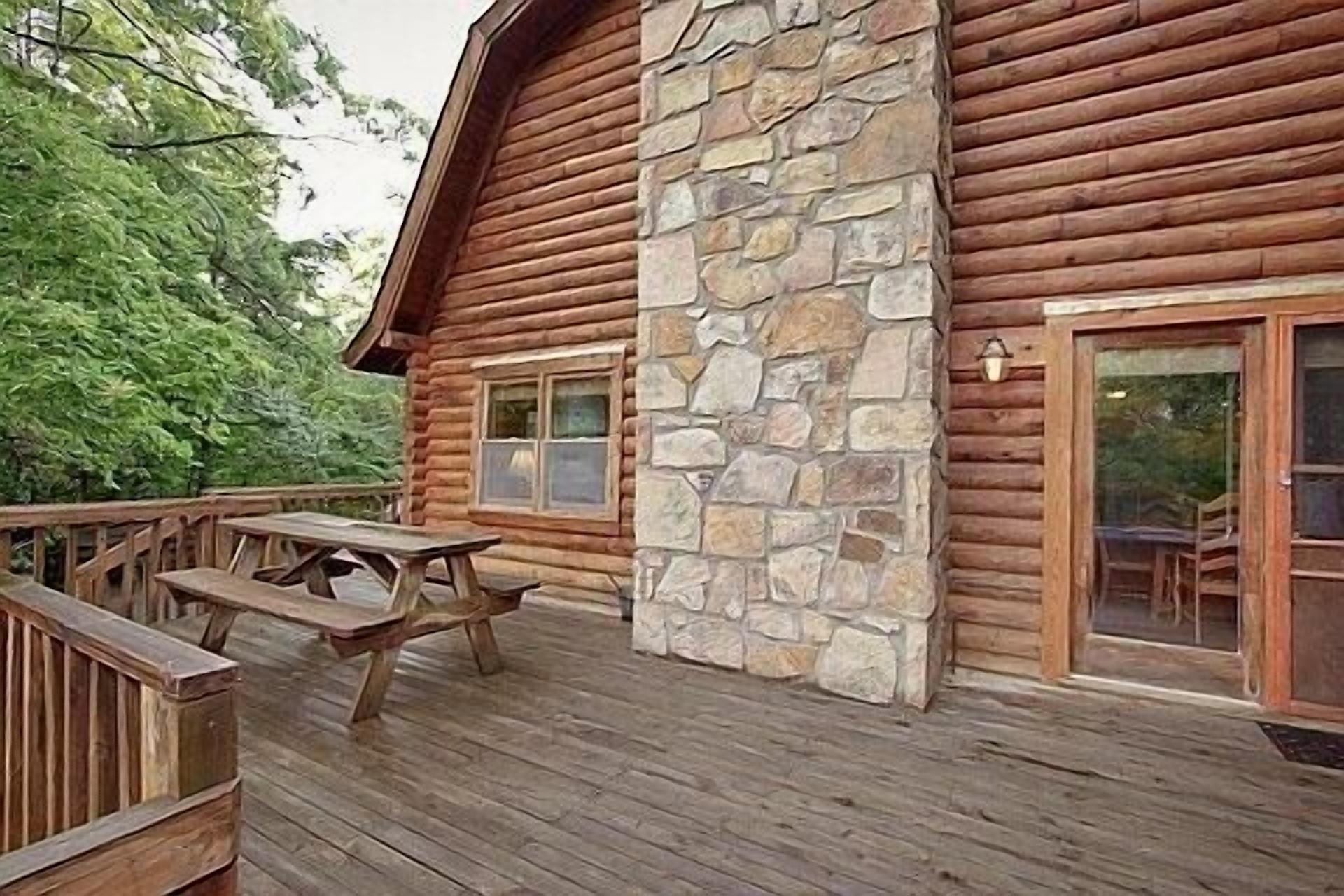 Une cabane en rondins avec une façade en pierre, une terrasse en bois et une table de pique-nique.