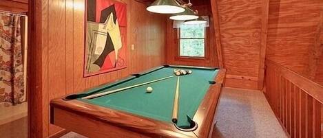 Una mesa de billar en una habitación de madera con un cuadro abstracto enmarcado en la pared y una ventana.