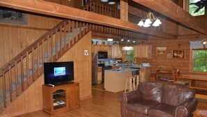 Un interior de madera con una escalera, un sofá de cuero, una zona de cocina y un televisor.