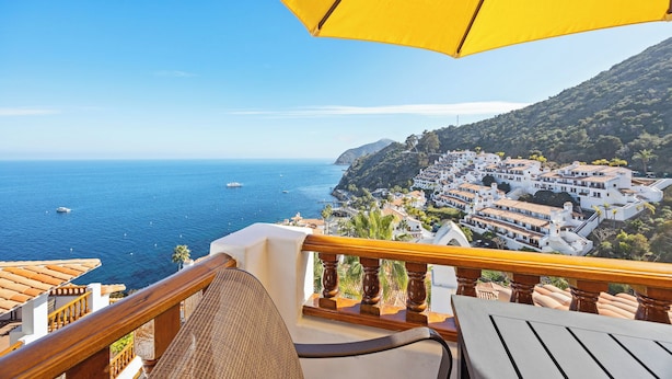 A balcony with a yellow umbrella, overlooking a coastal town with white buildings and the sea.