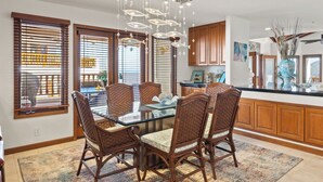 A dining area with a glass-top table and wicker chairs, wooden cabinets, and a hanging light fixture.