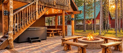 A wooden cabin with a staircase, outdoor seating, and a fire pit.
