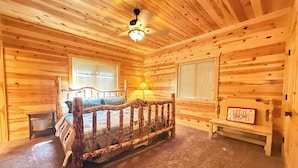 A log cabin room with a bed, a bench, a ceiling fan, and a sign that says 'LET IT SNOW'. - 22 MI to YNP | Firepit & Patio | Spacious Lodge (Island Park)