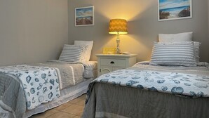 Une chambre avec deux lits, une table de chevet avec une lampe et deux tableaux encadrés au mur.