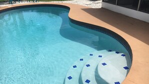 Une piscine à l’eau d’un bleu cristallin, aux bords incurvés et dotée d’une terrasse carrelée ornée de motifs en losanges bleus.