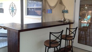 Un espace d’accueil avec un comptoir en bois, deux tabourets de bar, un mur décoratif orné d’un emblème en forme d’étoile et un panneau indiquant « RELAX ».