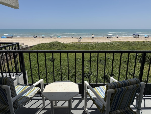 Un balcon avec vue sur la plage, comprenant une table et deux chaises à rayures.