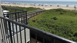 A beach with a wooden walkway leading to the shore, surrounded by greenery. - Oceanfront Studio, sleeps 4 -Private balcony, pool, hot tub, BBQ (South Padre Island)