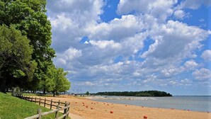A sandy beach with a wooden fence, trees, and a clear sky.
