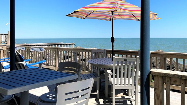 A wooden deck with a table and chairs, an umbrella, and a view of the ocean.
