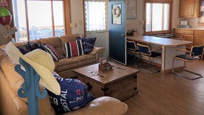 A cozy living room with a sofa, coffee table, and a dining area with a table and chairs. There is a kitchen area with cabinets and a refrigerator.